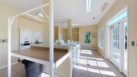 This single-floor communal laundry facility is designed with both functionality and comfort in mind. The space is generously lit by a combination of fluorescent overhead lighting and abundant natural light streaming through large windows, which also offer pleasant views of lush greenery outside. The warm beige walls and light tile flooring create a clean, welcoming atmosphere throughout.

The layout is thoughtfully organized, featuring multiple top-load washing machines arranged in rows alongside stacked washer-dryer units, providing ample capacity for residents. Sturdy folding counters with a tan laminate surface run along the sides of the room, offering convenient space for sorting and folding laundry. White support columns are integrated into the design, with hanging rods attached to provide additional utility for air-drying garments.

A framed informational notice is mounted near the windows, keeping users informed of facility guidelines. The tile flooring is easy to maintain and suited to the high-traffic nature of the space. Ceiling vents ensure proper ventilation, contributing to a fresh and comfortable environment. Overall, this laundry facility is a practical, well-maintained shared amenity that prioritizes user convenience and a pleasant experience.