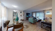 This single-floor residence offers a thoughtfully designed layout that balances open, communal spaces with private retreats. The entry opens directly into a dining area with wood-look flooring, where a glass-top table is bathed in natural light from a large window dressed with patterned drapes. The space flows seamlessly into a generously sized living room, anchored by a sliding glass door that leads to an outdoor patio and fills the room with abundant natural light. Wood-look flooring continues throughout the main living areas, complementing the neutral wall tones and textured ceilings.

The galley-style kitchen is outfitted with white cabinetry, granite-look countertops, a mosaic tile backsplash, and black appliances, offering efficient workspace along both sides of the corridor layout. The bedroom is a serene retreat featuring plush carpeting, a bold teal accent wall, ample natural light from a dedicated window, and access to a walk-in closet. Two bathrooms serve the residence, each finished with white cabinetry, granite-look countertops, and framed mirrors. The overall ambiance is modern and inviting, with a consistent design palette of cool blues, warm wood tones, and crisp whites throughout.