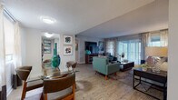 This single-floor residence offers a thoughtfully designed layout that balances open, communal spaces with private retreats. The entry opens directly into a dining area with wood-look flooring, where a glass-top table is bathed in natural light from a large window dressed with patterned drapes. The space flows seamlessly into a generously sized living room, anchored by a sliding glass door that leads to an outdoor patio and fills the room with abundant natural light. Wood-look flooring continues throughout the main living areas, complementing the neutral wall tones and textured ceilings.

The galley-style kitchen is outfitted with white cabinetry, granite-look countertops, a mosaic tile backsplash, and black appliances, offering efficient workspace along both sides of the corridor layout. The bedroom is a serene retreat featuring plush carpeting, a bold teal accent wall, ample natural light from a dedicated window, and access to a walk-in closet. Two bathrooms serve the residence, each finished with white cabinetry, granite-look countertops, and framed mirrors. The overall ambiance is modern and inviting, with a consistent design palette of cool blues, warm wood tones, and crisp whites throughout.