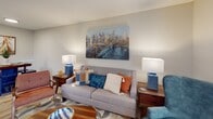 Located at 2950 E North St in Greenville, South Carolina, this single-story residence offers a thoughtfully designed layout with comfort and functionality at its core. The living room serves as a welcoming centerpiece, featuring neutral walls, a textured ceiling, and natural light filtered through blinds and decorative drapes. The space accommodates a comfortable seating arrangement accented by vibrant throw pillows and warm wood-toned furnishings. The kitchen is equipped with stainless steel appliances, including a refrigerator, electric range, and microwave, complemented by crisp white cabinetry and light wood-look flooring that extends throughout the main living areas. The primary bedroom is generously sized, featuring plush carpeting, a large window with ample natural light, and room for a full furniture arrangement. A secondary bedroom offers similar carpeted flooring, a bright window, and built-in wall shelving for added storage. The bathroom includes a vanity with quartz-style countertops, wood-look tile flooring, and a tub-shower combination. A dedicated laundry area with washer and dryer hookups adds everyday convenience, rounding out this well-equipped and move-in ready home.