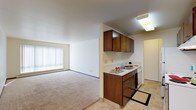 This single-floor residence offers a practical and comfortable layout designed for everyday living. The kitchen is efficiently arranged with rich dark wood cabinetry, light countertops, tile flooring, and a full suite of appliances including a stainless electric range, refrigerator, and dishwasher. A skylight above the sink area adds a touch of natural brightness to the space. The kitchen opens toward the living area, creating an easy flow between the two spaces. The living room is generously sized, featuring wall-to-wall carpeting, neutral cream-toned walls, and a large window dressed with vertical blinds that invites natural light while offering privacy. A baseboard heating system runs along the perimeter, ensuring warmth throughout. The bedroom is comfortably proportioned with soft carpeting, two windows that bring in natural light, and a wide reach-in closet with double hanging rods providing substantial storage. The full bathroom is clean and functional, featuring tile flooring, a single-sink vanity with a light countertop, a tub-shower combo, and wall-mounted lighting. Throughout the residence, the neutral color palette and consistent finishes create a cohesive, understated ambiance that is easy to personalize.