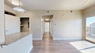 This well-appointed single-floor home offers three bedrooms, two bathrooms, and a thoughtfully designed layout that maximizes functionality. The combined kitchen and living area serves as the heart of the home, featuring wood-look flooring that extends through the main spaces and into the hallways. The kitchen is outfitted with rich dark cabinetry, granite-style countertops, a peninsula with additional counter space, and black appliances including a refrigerator, range, and dishwasher — providing ample storage and prep space. A hallway connects the main living area to the private quarters, maintaining a clear separation between shared and personal spaces. The living room benefits from a ceiling fan, sliding glass door access to an outdoor area, and generous natural light. Each bedroom is carpeted and features windows with blinds that allow natural light and exterior views. The primary bedroom includes a dedicated walk-in closet with built-in shelving and hanging rod. Both bathrooms echo the kitchen's design aesthetic with dark vanity cabinetry and granite-style countertops; the full bath includes a tiled tub-shower surround and wood-look flooring. The overall palette is neutral and clean, creating a bright, move-in-ready atmosphere throughout.