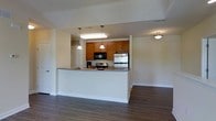 Located at 300 Autumn River Run in the Roxborough neighborhood of Philadelphia, PA, this single-floor residence offers a thoughtfully designed open-concept layout that maximizes both functionality and comfort. The kitchen serves as a central feature of the home, equipped with stainless steel appliances including a refrigerator and range, a built-in microwave, and warm honey-toned cabinetry that provides ample storage. A peninsula counter extends from the kitchen, creating a natural divide between the cooking area and the adjoining living space while offering additional prep and seating space. Pendant lighting above the peninsula adds a stylish, focused ambiance to the kitchen area. The living area is generously proportioned, featuring rich dark hardwood-style flooring that runs throughout, lending warmth and visual continuity to the space. Neutral wall tones keep the interior feeling bright and adaptable to a variety of furnishing styles. Recessed and flush-mount ceiling fixtures provide consistent lighting throughout. The overall design is clean, modern, and practical, with an open flow that makes the single-floor layout feel expansive and well-connected.