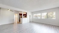 Located at 110 E Leatrice Ln in Anaheim, CA, this 2-bedroom, 1-bathroom home offers a thoughtfully arranged single-floor layout. The open-concept living room is a standout feature, showcasing light wood-style vinyl flooring, a textured ceiling, a ceiling fan, and large windows fitted with horizontal blinds that invite generous natural light and outdoor views. A wall-mounted AC unit provides climate control directly in the living space.

The kitchen is semi-open to the living area via a half-wall pass-through, offering dark wood cabinetry with a tile backsplash, stainless steel appliances including a refrigerator, gas range, and microwave, as well as a window above the counter for added ventilation and light.

Both bedrooms continue the light vinyl flooring and neutral white walls, each equipped with windows that bring in natural light. The primary bedroom includes a dedicated closet with a hanging rod for storage. The second bedroom offers a similarly bright and clean layout.

The full bathroom is clean and simply appointed, featuring a white vanity, toilet, and a bathtub with a shower. A connecting hallway links all rooms efficiently. Throughout the home, the consistent use of light tones and flooring creates a cohesive, bright, and welcoming atmosphere.