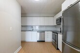 Located at 1319 Ouellette Ave in Windsor, Ontario, this one-bedroom, one-bathroom unit offers a thoughtfully organized single-floor layout. Light wood laminate flooring runs throughout the entire space, contributing to a clean, cohesive aesthetic complemented by neutral grey walls and white trim.

The combined kitchen and living area forms the heart of the unit. The kitchen is well-appointed with sleek white flat-front cabinetry extending to the ceiling, a white subway tile backsplash, grey countertops, and a full suite of stainless steel appliances including a French door refrigerator, electric range, over-the-range microwave, and dishwasher. The adjacent living area is bright and open, featuring a large window that frames views of mature trees along the street, along with a sliding glass door that leads directly to a private balcony.

The bedroom is a comfortable, well-proportioned room with a dedicated closet and a window that brings in natural light. The bathroom is finished in crisp white with tile flooring, a full soaker tub with shower, and clean, simple fixtures. Baseboard and panel heating units are present throughout. The tile ceiling panels add a distinctive character to the living and kitchen areas, rounding out this functional and well-maintained unit.