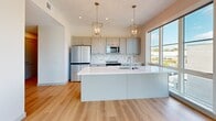 Located at 304 E Jackson Blvd in Elkhart, Indiana, this thoughtfully designed one-bedroom, one-bathroom unit offers a clean, modern aesthetic throughout its well-appointed floor plan. Light hardwood flooring flows seamlessly from room to room, complementing the bright white walls and gray-toned trim and doors.

The open-concept living, dining, and kitchen area serves as the heart of the unit. The kitchen is a standout, featuring gray shaker-style cabinetry, stainless steel appliances, a marble-look tile backsplash, and a large center island with a white quartz countertop and an undermount sink. Elegant gold-toned pendant lantern fixtures add a refined touch overhead. Oversized windows bathe the entire living and dining area in natural light while offering views of the surrounding neighborhood.

The spacious bedroom includes a ceiling fan, a large window with outdoor views, and a double-door closet, providing generous storage. An in-unit washer and dryer add everyday convenience. The bathroom features a light-toned vanity with a framed mirror, a walk-in shower, and continued hardwood-style flooring for a cohesive finish.

Throughout the unit, recessed lighting, clean lines, and a neutral color palette create a bright, contemporary atmosphere that is both functional and inviting.