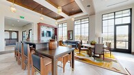 Located at 7395 E Legacy Blvd in Scottsdale, Arizona, this single-floor amenity facility offers a generous and thoughtfully designed space for fitness and community gathering. The layout encompasses two distinct exercise rooms and connecting hallways, delivering a comprehensive wellness experience.

The main fitness area is outfitted with commercial-grade equipment, including treadmills, stair climbers, cable machines, and a full dumbbell rack, all set atop large-format dark tile flooring. Floor-to-ceiling windows flood the space with natural light and frame sweeping outdoor views of the surrounding Scottsdale landscape. Tray ceilings with accent lighting and ceiling fans add architectural polish. A dedicated functional training room features hardwood-style flooring, a freestanding rig with TRX suspension trainers, kettlebells, and wall-mounted mirrors, offering a versatile space for dynamic workouts.

The communal hallway and gathering areas reflect a sophisticated interior design aesthetic, with coffered wood-beam ceilings, elegant pendant lighting, large-format tile floors, and vivid area rugs. A staircase with custom wrought-iron railings and vaulted ceilings with exposed wood beams enhances the grand, resort-style atmosphere. Warm wood tones, curated artwork, and a rich color palette contribute to a welcoming and upscale ambiance throughout.