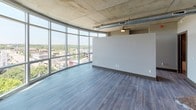 Located in the heart of downtown Kalamazoo at 227 W Michigan Ave, this single-floor unit showcases a distinctive industrial-modern design. The main living area is defined by a sweeping curved wall of floor-to-ceiling windows that flood the space with natural light and offer expansive views of the Kalamazoo skyline and surrounding treetops. Exposed concrete ceilings with visible ductwork reinforce the industrial aesthetic, while wood-plank flooring in a cool gray tone runs throughout the living and bedroom areas.

The kitchen is well-appointed with granite countertops, a mosaic tile backsplash, medium-toned wood cabinetry, and a full suite of stainless steel appliances, including a refrigerator, range, and microwave. A dual-basin sink with additional counter space provides ample room for meal preparation.

The bathroom features wood-look flooring, a granite-topped vanity with gray cabinetry, a full soaking tub with subway tile surround, and a window that brings in natural light. A dedicated in-unit laundry closet houses a stacked washer and dryer. Throughout the unit, the combination of raw architectural elements and refined finishes creates a cohesive, contemporary urban living environment.
