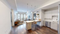 Located at 9 City Place in Nashville, Tennessee, this well-appointed two-bedroom, two-bathroom residence offers a thoughtfully designed single-level layout. The open-concept kitchen and living area serve as the heart of the home, where rich hardwood-style flooring flows throughout. The kitchen is outfitted with stainless steel appliances, white cabinetry, a large island with pendant lighting, and a tray ceiling that adds architectural interest. The living room is bright and inviting, with floor-to-ceiling French doors that welcome natural light and provide outdoor views. The primary bedroom features a bold geometric accent wall, plush carpeting, and large windows dressed with floor-length curtains. The second bedroom is equally well-lit, with neutral tones and natural light from a large window. A spacious walk-in closet with wire shelving provides generous storage. Both bathrooms are finished with wood-grain vanities, white quartz countertops, dark-framed mirrors, and hardwood-style flooring. One bathroom includes accessibility features such as grab bars. The overall ambiance is modern and comfortable, blending clean lines with warm finishes throughout.