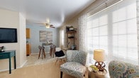 This single-floor residence offers a thoughtfully designed layout that balances comfort and functionality throughout. The living room serves as the heart of the home, featuring soft carpeted flooring, light blue walls, and a ceiling fan. Large windows dressed with patterned curtains flood the space with natural light, creating a bright and welcoming atmosphere. A wall-mounted television and open shelving add to the room's practical charm, while the adjacent dining area with tile flooring provides a seamless transition to the kitchen.

The kitchen is equipped with warm wood cabinetry, light countertops, a stainless steel sink, and essential appliances including a range and dishwasher. Tile flooring completes this functional space.

The primary bedroom is generously sized with plush carpeting, neutral walls, and a window that invites natural light. It is complemented by a walk-in closet and a private bathroom. A second bedroom, equally comfortable, also features carpet flooring and a window with outdoor views, offering a peaceful retreat.

The bathroom is clean and efficiently laid out, featuring a white vanity, tiled shower-tub combination, and tile flooring. Throughout the residence, a consistent neutral and soft color palette creates a calm, cohesive ambiance ideal for everyday living.