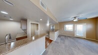 Located at 6885 W Lone Mountain Rd in Las Vegas, NV, this one-bedroom, one-bathroom unit offers a well-designed single-floor layout that maximizes functionality and comfort. The open-concept kitchen and living area serves as the heart of the home, where warm hardwood-style flooring transitions seamlessly from the kitchen into the living space. The kitchen is outfitted with rich wood cabinetry, granite countertops, stainless steel appliances including a gas range, built-in microwave, and refrigerator, providing ample workspace for cooking. A peninsula counter separates the kitchen from the living area, which features plush carpet, a ceiling fan, and a window that brings in natural light. The bedroom is a comfortable, carpeted retreat with multiple windows dressed in vertical blinds, a ceiling fan, and direct access to a dedicated closet and the full bathroom. The bathroom includes a granite-topped vanity, tile flooring, and a full tub/shower combination. A dedicated in-unit laundry area accommodates a full-sized washer and dryer. Warm neutral tones throughout the unit create a cohesive and inviting atmosphere.