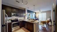 Located at 501 Willard St in Durham, NC, this single-floor residence offers a well-appointed, open-concept layout designed for comfortable modern living. The kitchen is a standout feature, equipped with stainless steel appliances including a refrigerator, range, and over-the-range microwave, complemented by rich dark cabinetry, granite countertops, a subway tile backsplash, and wood-look flooring. A central island with a double sink and pendant lighting above doubles as a breakfast bar with seating, connecting seamlessly to the living area. The living room features a bold navy accent wall, a ceiling fan, and a large sliding glass door that fills the space with natural light and provides outdoor access. The primary bedroom is carpeted and includes an en-suite bathroom with granite vanity, dark cabinetry, and a shower-tub combination. A second bedroom features its own striking navy accent wall, carpet flooring, a ceiling fan, natural window light, and a walk-in closet. A third, cozier bedroom offers neutral tones and natural light. A second full bathroom with granite countertops and a tub-shower combination serves the additional bedrooms. The overall aesthetic blends contemporary finishes with warm, inviting tones throughout.