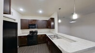 This single-story residence offers a thoughtfully organized layout with distinct living, sleeping, and functional zones connected by a clean, open corridor. The kitchen serves as a central highlight, outfitted with rich dark espresso cabinetry, light stone-look countertops, and black appliances including a range, over-the-range microwave, and refrigerator. A double-basin stainless steel sink sits beneath pendant lighting, which also illuminates a breakfast bar peninsula that transitions into the main living area. Recessed lighting and wood-look plank flooring carry throughout the kitchen, hallway, and living space, lending a cohesive, modern feel.

The living area is open and bright, featuring a ceiling fan, recessed lighting, and a window allowing natural light. A hallway connects the space to multiple bedrooms, each finished with plush wall-to-wall carpeting, ceiling fans, and panel doors leading to closets. One bedroom benefits from a window with exterior views.

Two bathrooms are present, each featuring a tiled tub-shower combination with chrome fixtures, wood-look flooring, and dark vanity cabinetry. The overall aesthetic is clean, neutral, and move-in ready.