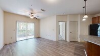 Located at Two Addison Place in Pooler, Georgia, this single-floor residence offers a thoughtfully designed layout with a clean, neutral aesthetic throughout. The living area features wood-look plank flooring and a ceiling fan, with a sliding glass door fitted with vertical blinds that allows abundant natural light and provides access to an outdoor space with views of surrounding greenery.

The kitchen is a functional highlight, equipped with warm medium-tone wood cabinetry, granite countertops, a double-basin stainless steel sink, and black appliances including a refrigerator, dishwasher, range, and over-the-range microwave. A curved granite-topped island adds additional prep and serving space, seamlessly connecting the kitchen to the living areas.

The bedrooms feature plush carpeting and ceiling fans, with multiple windows dressed in horizontal blinds that invite natural light. The rooms offer generous proportions suited for comfortable furnishing arrangements. A hallway connects the private areas of the home, finished with the same wood-look flooring found in the main living spaces.

The bathroom includes a wood-toned vanity with granite countertop, consistent with the design language seen throughout the home. Overall, the space presents a cohesive, move-in ready interior with durable finishes and a light, airy ambiance.