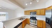 Located at 4400 Cortina Cir in Fort Myers, Florida, this single-floor residence offers a practical and comfortable layout with one bedroom and one bathroom. The kitchen is a functional highlight of the home, featuring warm honey-toned oak cabinetry, stainless steel appliances including an electric range, built-in microwave, and dishwasher, light stone countertops, a double-basin sink, and track lighting set beneath notably high ceilings that lend an open, airy feel to the space. Light tile flooring runs throughout the kitchen and extends into much of the home. The combined dining and living area provides a versatile, open space anchored by a ceiling fan with light fixture. The spacious primary bedroom is comfortably sized and also features a ceiling fan. The full bathroom is well-appointed with a dual-sink vanity with oak cabinetry, a large mirror, tile-surround soaking tub and shower, and tile flooring. A dedicated laundry area includes a stacked washer and dryer unit for added convenience. The residence also offers three closets for generous storage, a welcoming entrance, a hallway connecting the rooms, and a private patio for outdoor enjoyment.