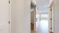 Located at 1130 Hazeltine Boulevard in Chaska, MN, this one-bedroom, one-bathroom residence offers a thoughtfully designed layout that maximizes every square foot. The open-concept living and kitchen area is anchored by light wood-style flooring that flows throughout the main living spaces, creating a bright and cohesive feel. Natural light enters through large windows, enhancing the airy, welcoming ambiance.

The kitchen is a standout feature, equipped with contemporary wood-grain cabinetry in a rich gray-brown tone, stainless steel appliances including a refrigerator, range, over-the-range microwave, and dishwasher, complemented by crisp white quartz countertops and a classic white subway tile backsplash. Recessed lighting adds a polished finishing touch overhead.

A stylish sliding barn door with matte black hardware separates the bedroom from the main living area, adding a modern design element. The carpeted bedroom provides a cozy retreat with ample wall space and direct access to the hallway and closet.

The bathroom features a wood-grain vanity with white countertop, a full soaking tub with shower, and clean white finishes throughout, accented by matte black fixtures and hardware. A dedicated hallway connects all rooms, contributing to an efficient and functional floor plan throughout this well-finished residence.
