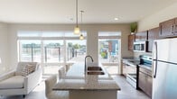 This well-appointed single-floor residence offers a thoughtfully designed open-concept layout with light wood-style flooring throughout. The kitchen serves as the heart of the home, showcasing a large granite-topped island with an undermount sink, rich dark wood cabinetry, stainless steel appliances including a refrigerator, electric range, and built-in microwave, all illuminated by stylish pendant lighting. Large windows overlooking an outdoor amenity area flood the kitchen and adjacent living spaces with natural light.

The living room is bright and welcoming, featuring expansive windows with views of the surrounding landscape and a sliding glass door that further enhances the connection to the outdoors. A dedicated home office space provides a quiet retreat, complete with a wide window offering views of the outdoor amenity area.

The bedrooms are comfortably sized, each benefiting from generous windows that bring in natural light and outdoor views. The space includes two bathrooms: a full bath with a tub-shower combination, granite vanity, and wood cabinetry, as well as a half bath with matching finishes. Consistent neutral tones, clean lines, and modern fixtures create a cohesive and contemporary ambiance throughout.
