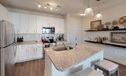 Located at 101 E Romana St in downtown Pensacola, Florida, this single-floor residence offers a thoughtfully designed layout with modern finishes throughout. The open-concept living area is bright and welcoming, featuring wood-look flooring, a ceiling fan, and large windows with a glass door that invites natural light and provides access to an outdoor balcony with views of the surrounding greenery. The kitchen is a standout feature, equipped with crisp white shaker cabinetry, a white subway tile backsplash, granite countertops, stainless steel appliances, and a generous island with bar seating and a built-in sink, illuminated by stylish pendant lighting. The primary bedroom is a comfortable retreat with plush carpeting, a ceiling fan, and large windows that frame outdoor views. Its en-suite bathroom features a granite-topped vanity, tile flooring, and leads directly to a walk-in closet with built-in shelving. A second bedroom offers similar comfort, with carpeted floors, a window with natural light, and ample wall space. The overall ambiance of the space is clean and contemporary, with neutral tones and consistent quality finishes that create a cohesive and functional living environment.