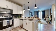 This thoughtfully designed 1-bedroom, 1-bathroom residence offers a functional and stylish single-floor layout. The open-concept kitchen is a standout feature, boasting white shaker cabinetry extending to the ceiling, a dark subway tile backsplash, stainless steel appliances, and a central island with a sink and pendant lighting — ideal for both cooking and casual dining with bar seating. Light wood-tone flooring flows seamlessly throughout the space, enhancing the cohesive modern aesthetic.

The living room is bright and welcoming, with a ceiling fan, room for a sectional seating arrangement, and direct access to an outdoor patio through a glass door framed by floor-length curtains. The bedroom features large windows that fill the room with natural light, a ceiling fan, and ample space for a king-sized bed. An adjacent bathroom offers a wide vanity with a gray quartz countertop, white cabinetry, and a tiled shower, with direct access to a dedicated walk-in closet fitted with built-in shelving and hanging rods. The entryway hallway includes open shelving for display and storage, completing this efficiently planned and contemporary residence.