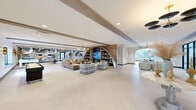 Located at 500 E Constitution Dr in Palatine, IL, this single-floor community amenity space offers a generously sized, thoughtfully designed environment built for socializing, recreation, and relaxation. The open layout flows seamlessly across multiple functional zones, all unified by light terrazzo-style flooring, recessed lighting, and warm wood beam accents throughout the ceiling.

The main lounge area is a standout, featuring a striking botanical mural in blues and golds that anchors the space alongside a cozy fireplace, built-in shelving, and a wall-mounted TV. Curved seating, an arched wood bookshelf display unit, and curated décor give the area a contemporary yet welcoming character. Large windows throughout flood the interior with natural light and offer views of the surrounding greenery.

A dedicated game room includes a ping-pong table, foosball table, pool table, and arcade games, all set against bold, artistic wall treatments. A separate dining area features a substantial conference-style table beneath a statement pendant light, framed by floor-to-ceiling windows with pool views. A glass-enclosed fitness center with strength training equipment is also accessible directly from the main corridor, rounding out this well-appointed community facility.