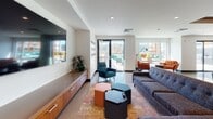 This contemporary single-floor space is defined by clean lines, an open-plan layout, and a cohesive modern aesthetic that flows seamlessly from room to room. Polished concrete floors run throughout, reflecting natural light and lending a refined industrial character to the interior.

The kitchen is a standout feature, outfitted with rich wood-grain cabinetry that extends from floor to ceiling, offering generous storage alongside open display shelving. A sleek grey countertop runs the length of the wall, complemented by a stainless steel sink and built-in appliances. A central island provides additional workspace and casual seating.

The lounge area is generously proportioned, anchored by a large wall-mounted flat-screen television above a low-profile wood media console that echoes the cabinetry style found throughout. Comfortable sectional seating, eclectic accent chairs, and colorful hexagonal ottomans create an inviting, relaxed atmosphere. A vibrant area rug adds warmth and contrast to the polished floors. Large sliding glass doors open directly to an outdoor terrace, flooding the space with natural light and providing seamless indoor-outdoor connectivity.

A dedicated office or workroom features the same warm wood built-ins and polished floors, accented by bold artwork that adds personality. Throughout the space, curated art pieces contribute to a distinctive, character-rich environment that balances functionality with contemporary design.