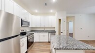 This thoughtfully designed single-floor residence offers a comfortable and functional layout with 1 bedroom and 1 bathroom. The open-concept kitchen and living area serves as the heart of the home, anchored by a kitchen outfitted with crisp white shaker cabinetry, granite countertops, a central island, and a full suite of stainless steel appliances including a refrigerator, electric range, over-the-range microwave, and dishwasher. Warm wood-look flooring runs throughout the entire unit, lending a cohesive and inviting feel. The living area features a ceiling fan and French doors that open to the outside, bringing in natural light and providing convenient outdoor access. The spacious primary bedroom includes its own ceiling fan, a window for natural light, and direct access to a generous walk-in closet equipped with wire shelving. The bathroom is clean and modern, featuring a sliding glass walk-in shower and wood-look flooring. A dedicated laundry room houses a full-size top-loading washer and dryer. Additional conveniences include a pantry, a utility room, multiple closets for storage, and a hallway connecting the living spaces. The overall aesthetic is fresh, bright, and move-in ready.