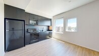 Located at 270 N Hancock St in Portland's vibrant Boise neighborhood, this efficiently designed single-floor unit offers a thoughtfully organized open-concept layout. Light-toned luxury vinyl plank flooring runs throughout the main living areas, creating a cohesive and easy-to-maintain foundation.

The kitchen is a standout feature, outfitted with sleek dark cabinetry extending to the ceiling, stainless steel appliances including a refrigerator, electric range, over-the-range microwave, and dishwasher. A double-basin sink and continuous dark backsplash complete the contemporary look. Large windows adjacent to the kitchen invite abundant natural light and frame views of the surrounding Portland cityscape.

The open living area benefits from a ceiling fan and multiple windows along one wall, further brightening the space and providing additional city views. A dedicated sleeping area includes a spacious sliding-door closet, offering practical storage.

A separate laundry closet houses a stacked washer and dryer, adding convenience. The bathroom features tile-style flooring, a vessel-style sink, and clean white walls accented with matte black hardware. An entry hallway connects all areas of the unit seamlessly. The overall design aesthetic is clean, modern, and functional, well-suited for everyday urban living in Portland.