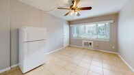 This 250 square foot studio apartment in Saint Petersburg, Florida, maximizes its compact footprint with an efficient layout. The space features a single floor plan that incorporates a kitchen, bathroom, and closet. 

The main living area is characterized by neutral-toned walls and large windows that allow natural light to flood the space. A ceiling fan with wooden blades adds both functionality and a touch of warmth to the room. The floors throughout the apartment are covered in beige ceramic tiles, providing a clean and low-maintenance surface.

The kitchen, though small, is well-equipped with white cabinetry, a compact range, and a sink. It's designed to maximize utility in a limited space. Adjacent to the kitchen, there's a closet area for storage.

The bathroom features a bathtub-shower combination with sunny yellow tiles that add a cheerful pop of color to the space. White fixtures and chrome fittings complete the bathroom's functional yet bright aesthetic.

A window-mounted air conditioning unit is visible, ensuring climate control in Florida's warm weather. The apartment's layout, while compact, offers a practical living solution for those seeking an efficient urban dwelling in Saint Petersburg.
