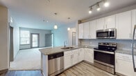 This well-appointed single-floor residence offers a thoughtfully designed open-concept layout that seamlessly connects the kitchen and living area. The kitchen is a standout feature, showcasing crisp white cabinetry, granite countertops, a subway tile backsplash, and a full suite of stainless steel appliances including a refrigerator, electric range, microwave, and dishwasher. Pendant lighting above the kitchen island adds a stylish touch, while track lighting illuminates the workspace. Light wood-style flooring runs throughout the kitchen and extends into the hallways, complementing the neutral color palette.

The open living area transitions to soft carpeting and is bathed in natural light from a large window and a glass-paneled exterior door. The bedrooms continue the carpeted flooring and feature ample natural light, ceiling fans, and generous closet space, including a walk-in closet with wire shelving. 

The primary bathroom is notably spacious, offering a dual-sink vanity topped with granite, white cabinetry, framed mirrors, and wood-look flooring. A separate water closet provides added privacy. Throughout the residence, neutral tones, clean lines, and consistent finishes create a cohesive, modern ambiance.
