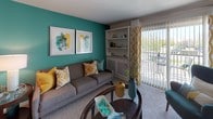 This single-floor residence is thoughtfully laid out to maximize functionality and comfort across its key living areas. The living room serves as the central gathering space, featuring plush carpeting, a bold teal accent wall adorned with framed artwork, and a built-in shelving unit. A sliding glass door provides direct access to an outdoor balcony, allowing natural light to fill the room.

Adjacent to the living room, the dining area accommodates a round table with seating for four, enhanced by a ceiling fan overhead and a pass-through connection to the kitchen. The kitchen is equipped with warm oak cabinetry, ample counter space, and white appliances including a range, dishwasher, refrigerator, and built-in microwave, all set on light tile flooring.

The residence includes two bedrooms, each featuring ceiling fans, carpet flooring, and accent walls in soothing teal tones. One bedroom benefits from a large window with outdoor views, while the other offers a quieter, more neutral setting. Both bathrooms include a tub-shower combination with tile surround and clean, functional finishes throughout.