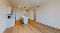 Located in Philadelphia's vibrant South Philly neighborhood, this modern single-floor unit at 1331 S Juniper Street showcases a clean, contemporary design with high-quality finishes throughout. The open-concept living and kitchen area is anchored by light-toned hardwood flooring that flows seamlessly from room to room, creating a cohesive and airy atmosphere.

The kitchen is a standout feature, equipped with a large center island topped with white quartz countertops and a matte black undermount sink. White cabinetry with black hardware pairs with a classic subway tile backsplash, and stainless steel appliances — including a refrigerator, range, and built-in microwave — complete the space. A sleek linear pendant light adds a modern touch overhead.

The living area opens directly to city views through full-height sliding glass doors, allowing an abundance of natural light to fill the space. Additional bedrooms feature wide windows overlooking the Philadelphia roofscape, continuing the theme of brightness and openness.

The bathrooms are thoughtfully finished, with one featuring large-format dark tile flooring, a glass-enclosed walk-in shower with subway tile surround, and matte black fixtures. A second bathroom offers a soaking tub with matching subway tile and neutral tile flooring. Both bathrooms maintain a clean, minimalist aesthetic consistent with the overall design of the unit.