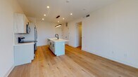 Located in Philadelphia's vibrant South Philly neighborhood, this modern single-floor unit at 1331 S Juniper Street showcases a clean, contemporary design with high-quality finishes throughout. The open-concept living and kitchen area is anchored by light-toned hardwood flooring that flows seamlessly from room to room, creating a cohesive and airy atmosphere.

The kitchen is a standout feature, equipped with a large center island topped with white quartz countertops and a matte black undermount sink. White cabinetry with black hardware pairs with a classic subway tile backsplash, and stainless steel appliances — including a refrigerator, range, and built-in microwave — complete the space. A sleek linear pendant light adds a modern touch overhead.

The living area opens directly to city views through full-height sliding glass doors, allowing an abundance of natural light to fill the space. Additional bedrooms feature wide windows overlooking the Philadelphia roofscape, continuing the theme of brightness and openness.

The bathrooms are thoughtfully finished, with one featuring large-format dark tile flooring, a glass-enclosed walk-in shower with subway tile surround, and matte black fixtures. A second bathroom offers a soaking tub with matching subway tile and neutral tile flooring. Both bathrooms maintain a clean, minimalist aesthetic consistent with the overall design of the unit.
