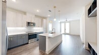 This well-appointed 2-bedroom, 3-bathroom single-floor residence offers a thoughtfully designed open-concept layout with modern finishes throughout. The combined kitchen and living area serves as the heart of the home, featuring a central island with a built-in sink, sleek white quartz countertops, and dual-tone cabinetry with light upper cabinets and slate-blue lower cabinets accented by gold hardware. Stainless steel appliances, a white subway tile backsplash, and globe pendant lights with brass fixtures add a contemporary touch. The living area extends seamlessly from the kitchen, bathed in natural light from French doors and is equipped with a ceiling fan. Wide-plank wood-look flooring runs throughout the entire space, providing a cohesive aesthetic. The two bedrooms are bright and airy, each featuring large windows with views of the surrounding area, ceiling fixtures, and neutral wall tones. The primary bedroom includes a dedicated closet with built-in shelving and hanging rods for organized storage. The bathrooms are finished to a high standard, with at least one featuring a walk-in glass-enclosed shower with large-format tile, a built-in niche, and a bench seat. Two hallways and two closets complete the functional layout of this well-designed residence.