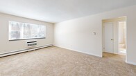 Located at 209 Pleasant Street in Melrose, MA, this two-bedroom, two-bathroom residence offers a practical and well-organized single-floor layout. The combined living and dining area is generously proportioned, featuring wall-to-wall carpeting, baseboard heating, a wall-mounted A/C unit, and a large window that allows natural light to fill the space. The kitchen is thoughtfully designed with white cabinetry accented by warm wood trim, a gas range, dishwasher, stainless steel sink, and durable hardwood flooring — providing a clean and functional cooking environment. Both bedrooms are carpeted and bright, each featuring windows with outdoor views and access to closet storage. The primary bedroom is notably spacious and includes a double louvered closet, offering ample storage. With four closets total throughout the unit, storage is plentiful. The bathroom features classic tilework with a basket-weave tile floor, tile wainscoting, a soaking tub with shower, and a vanity with a lighted mirror above. A hallway connects the rooms, contributing to a smooth and logical flow throughout. Baseboard heating is present throughout the unit, ensuring consistent comfort year-round.