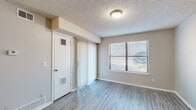 This single-story unit offers a practical and cohesive layout designed for comfortable everyday living. Consistent light gray wood-look flooring flows throughout the main living areas, complemented by neutral warm-beige walls and textured ceilings that give the space a clean, uniform appearance.

The living area is open and well-proportioned, featuring a sliding glass door fitted with vertical blinds alongside a window with horizontal blinds, allowing for generous natural light and outdoor views. A separate entry area provides convenient access and additional storage options.

The galley-style kitchen is efficiently arranged with ample white cabinetry above and below the counter, light speckled countertops, and a full suite of black appliances including a refrigerator, electric range, and dishwasher. Two windows provide natural light, keeping the kitchen bright and functional.

The bedroom features plush neutral carpeting and a ceiling fan with an integrated light fixture, enhancing comfort and air circulation. A window with blinds provides natural light.

The bathroom is cleanly appointed with a white vanity offering generous cabinet storage, a speckled countertop, a large mirror with a multi-bulb light bar above, and a full soaking tub with a shower surround. The wood-look flooring carries through into this space, maintaining a consistent aesthetic throughout the unit.