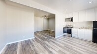 Located at 6921 Lewiston Way in Sacramento, CA, this single-story, one-bedroom, two-bathroom unit offers a thoughtfully designed layout that maximizes every square foot. The open-concept living and kitchen area is anchored by light gray hardwood-style flooring that runs seamlessly throughout the entire space, creating a cohesive and modern aesthetic.

The kitchen is well-appointed with crisp white cabinetry extending to the ceiling for ample storage, stainless steel appliances including an electric range with oven, over-the-range microwave, and a black refrigerator, plus a clean white sink and countertops. Recessed lighting illuminates the kitchen area efficiently.

The living room flows naturally from the kitchen through an arched opening, featuring a ceiling fan and a window that brings in natural light. The bedroom is a comfortable size, complete with a ceiling fan, a wall-mounted thermostat panel, and large sliding closet doors that provide generous storage.

The bathrooms are a standout feature, showcasing elegantly veined marble-look wall surrounds in the tub-shower combination, paired with hardwood-style flooring, recessed lighting, and clean white fixtures. The overall palette of soft grays, white trim, and neutral tones gives this unit a fresh, contemporary feel throughout.