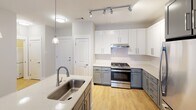 Located at 5820 Market Way Dr in Charlotte, NC, this single-floor residence offers a thoughtfully designed open-concept layout with contemporary finishes throughout. Light wood-look flooring flows seamlessly across the entire unit, creating a cohesive and inviting atmosphere.

The kitchen serves as a central focal point, showcasing a two-tone cabinetry scheme with crisp white upper cabinets and slate-gray lower cabinets paired with stainless steel appliances, including a gas range and french door refrigerator. A large center island with a quartz-style countertop and an undermount sink adds both prep space and functionality. Pendant lighting and track lighting illuminate the workspace, while the open design transitions naturally into the living area, which benefits from natural light through a window fitted with blinds.

The bedroom features light wood flooring, a ceiling fan, and a window providing natural light. A walk-in closet with built-in shelving offers generous storage. The bathroom is finished with white cabinetry, a dark countertop vanity with an undermount sink, a large mirror, and a tiled shower. Clean neutral wall tones and consistent trim work throughout the unit contribute to a polished, modern aesthetic.