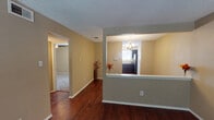 This single-story home offers a practical and cohesive layout designed for comfortable everyday living. The main living and dining areas are unified by rich, dark hardwood flooring that runs throughout, complemented by neutral warm-toned walls and textured ceilings. A defining architectural feature is the half-wall pass-through that connects the dining area to the kitchen, topped with a white ledge that promotes an open, connected feel while maintaining a sense of separation between spaces. An elegant chandelier hangs above the dining area, adding a refined touch to the space.

The kitchen is well-appointed with dark cabinetry, dark granite-style countertops, a double stainless steel sink beneath a window that allows natural light to filter in, and a stainless steel refrigerator. The cabinetry provides ample storage, and the window overlooks greenery outside.

The bedrooms feature plush carpeting, neutral wall tones, and ceiling fans with integrated lighting, creating a comfortable and restful atmosphere. Each room offers closet access, with bifold doors visible in at least one bedroom. Natural light enters through window treatments with horizontal blinds.

The bathroom is finished with a dark vanity cabinet, granite-style countertop, a single basin sink, a large mirror with overhead lighting, and a tub-shower combination. The consistent use of dark fixtures and cabinetry throughout ties the home's interior design together cohesively.