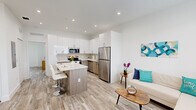 Located at 175 SW 7th Ave in Florida City, Florida, this well-appointed single-floor residence offers three bedrooms, two bathrooms, and a thoughtfully designed open-concept layout. Light wood-style flooring flows seamlessly throughout the home, creating a cohesive and airy aesthetic.

The kitchen is a standout feature, boasting high-gloss white upper cabinetry, warm wood-toned lower cabinets, and a striking marble-patterned quartz backsplash and countertops. A full suite of stainless steel appliances — including a refrigerator, range, microwave, and dishwasher — completes this functional and stylish space. A kitchen island with seating provides an ideal spot for casual dining and opens directly into the living area, enhancing the open flow of the home.

The primary bedroom is generously sized, featuring sliding glass door access and clean, bright finishes. A walk-in closet with wire shelving and hanging rods offers practical storage. The secondary bedrooms are bright and comfortable, each with natural light from well-placed windows. Both bathrooms are finished in neutral toned tile, with the full bath featuring a tub-shower combination and clean wood-accented vanity. Recessed lighting throughout contributes to the modern, polished ambiance of this Florida City residence.