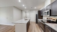 This single-story home in Saint Marys, Georgia offers a clean, modern design with a thoughtful layout across two bedrooms, two bathrooms, and two closets. Light wood-style flooring runs consistently throughout the entire home, lending a cohesive and contemporary feel to every room.

The open-concept kitchen and living area serves as the heart of the home. The kitchen is well-equipped with dark cabinetry, granite-style countertops, stainless steel appliances including a refrigerator, electric range, and microwave, and a central island with a double sink — ideal for both cooking and casual dining. Recessed lighting brightens the space, which flows naturally into the adjoining living area.

The bedrooms are comfortably sized, with neutral gray walls, white panel doors, and ample natural light from windows with blinds. Ceiling fans provide additional comfort. Each bedroom includes access to a closet, with one bedroom featuring a dedicated walk-in closet with wire shelving.

Both bathrooms are finished consistently with granite-top dark vanities, tub-shower combinations with white surrounds, and brushed nickel fixtures set against light, neutral walls. The overall ambiance of the home is clean, move-in ready, and well-suited for comfortable everyday living in a quiet Georgia coastal community.