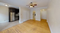 This single-floor unit combines classic charm with modern updates, offering a comfortable and functional living environment. The main living area is bright and open, showcasing warm hardwood floors, elegant crown molding, and a ceiling fan with integrated lighting. A bank of windows along one wall floods the space with natural light, while a traditional cast-iron radiator adds a touch of vintage character. Crown molding frames the room, enhancing its classic architectural appeal.

The kitchen is efficiently designed with a galley-style layout, featuring dark espresso cabinetry, light tile flooring, and a full suite of stainless steel appliances, including a refrigerator, electric range, and microwave. Ample upper and lower cabinetry provides generous storage throughout.

The layout flows seamlessly between spaces, with the living area connecting directly to the kitchen and additional rooms via a central corridor. A closet off the main living area offers convenient storage.

The bathroom is clean and well-maintained, featuring a glass-enclosed shower and tub combination with white subway tile, a white vanity with a medicine cabinet mirror, and modern brushed nickel fixtures. The overall aesthetic throughout the unit is neutral and inviting, making it a versatile and move-in ready space.