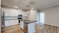 This well-appointed 3-bedroom, 2-bathroom single-story home offers a thoughtfully designed open-concept layout. The kitchen serves as a focal point, featuring crisp white cabinetry, dark granite countertops, a subway tile backsplash, and a full suite of stainless steel appliances including a gas range, microwave, and dishwasher. A central island with an integrated sink and matching granite top provides additional prep space and seating. Globe pendant lights add a modern touch overhead. Light wood-style plank flooring flows through the kitchen and living areas, while the living room benefits from natural light through a glass-paneled entry door and sidelights, complemented by a ceiling fan. One bedroom features a built-in desk with dark granite surface and white upper cabinetry — ideal as a home office. The carpeted bedrooms offer ceiling fans and windows with outdoor views. Each bedroom is supported by well-sized closets with built-in shelving and hanging rods. The bathrooms are finished with white vanity cabinetry, dark granite counters, and a glass-enclosed walk-in shower adorned with marble-style tile. Neutral warm tones and clean finishes throughout create a bright, cohesive ambiance.