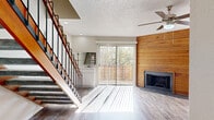 This two-story home offers a thoughtfully designed layout spread evenly across two floors, providing a comfortable balance of living and private spaces. The main level opens into a bright living area with light wood-look flooring, a textured ceiling, and a ceiling fan. A striking wood-paneled accent wall frames a classic fireplace, adding warmth and character to the space. Large sliding glass doors flood the room with natural light and offer views of the outdoors. The open-concept layout flows seamlessly into the dining area and a galley-style kitchen, which features white cabinetry, quartz countertops, stainless steel appliances including a refrigerator, range, microwave, and dishwasher, and a pass-through breakfast bar. A staircase with a warm wood and metal railing leads to the upper level, where the two bedrooms are located. The primary bedroom is generously sized, featuring a ceiling fan, a built-in window seat, and direct access to a private bathroom. Additional bathrooms — four in total — are clean and bright, with white tile surrounds and tub-shower combinations. A dedicated utility room and two closets provide practical storage solutions throughout the home. Light neutral tones and consistent flooring unify the space with a clean, modern aesthetic.
