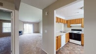 This single-floor residence offers a practical and comfortable layout with a neutral color palette throughout. The open-concept living and dining area is anchored by vaulted ceilings and a chandelier, creating an airy, spacious feel. A corner fireplace adds warmth and character to the living space, which is bathed in natural light from a large sliding glass door that opens to an outdoor balcony with views of surrounding greenery.

The kitchen is thoughtfully designed with warm oak cabinetry, ample upper and lower storage, a double sink, a dishwasher, an electric range, and a full-size refrigerator. Tile flooring in the kitchen provides a durable contrast to the plush carpeting found throughout the rest of the residence. A pass-through window connects the kitchen to the dining area, enhancing the open flow between spaces.

The hallway leads to the bedroom areas, each carpeted for comfort. The primary bedroom features direct access to a full bathroom equipped with a single-sink vanity, a tiled tub-shower combination, and tile flooring. Additional closet space is accessible along the main corridor. Overall, the space delivers a functional and inviting environment with consistent finishes and well-connected living areas.