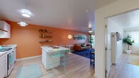 Located at 39869 Fremont Blvd in Fremont, California, this single-floor unit presents a thoughtfully designed layout with a cohesive, colorful aesthetic throughout. Light wood-style flooring flows consistently across the space, lending a warm, unified feel to each area.

The open-plan living and dining zone serves as the heart of the unit. A bold terracotta-orange accent wall provides a striking backdrop for the living area, where a tan leather sofa, a geometric navy area rug, and a large panoramic wall canvas contribute to an eclectic, curated atmosphere. A sliding glass door opens to a private patio, bringing in natural light and outdoor access. Adjacent to this is the dining area, anchored by a white kitchen island with aqua bar stools and wall-mounted shelving.

The kitchen features white cabinetry extending to the ceiling, a gas range, dishwasher, refrigerator, and a range hood, offering practical functionality in a clean, minimal design.

The bedroom is finished with a soft blue accent wall and light-filtering curtains that allow ample natural light. A walk-in closet provides generous storage. The bathroom is crisp and modern, with a white vanity, bold geometric black-and-white tile flooring, and a glass-enclosed walk-in shower with matte black fixtures.