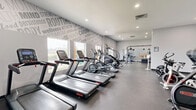 Located at 515 John Muir Drive in San Francisco, this single-floor fitness facility offers a comprehensive workout environment spread across a generously sized footprint. The space is divided into two distinct areas: a fully equipped exercise room and a flexible game room, together accommodating a wide variety of fitness activities.

The exercise room is a standout feature, outfitted with an extensive array of cardio and strength-training equipment, including treadmills, ellipticals, stationary bikes, a StairMaster, cable machines, and free weights. Large windows flood the space with natural light while providing outdoor views, and bold typographic murals featuring fitness-themed words energize the walls throughout. Recessed lighting and durable rubber flooring complete the modern, motivating aesthetic.

The game room serves as a versatile studio space, featuring wall-to-wall mirrors, a ballet barre, a wall-mounted flat-screen TV, and open rubber flooring ideal for group fitness classes, dance, or functional training. Colorful word-art murals line the upper walls, reinforcing the health-focused atmosphere. A small trampoline, kettlebells, dumbbells, and other portable equipment are also available within the studio.

Together, these two areas create a well-rounded fitness center that is both functional and visually inspiring, designed to motivate users at every fitness level.