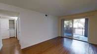 This single-floor space offers a clean, functional layout highlighted by warm hardwood flooring that extends throughout the main living area. The room is finished with crisp white walls and white trim, creating a bright and neutral backdrop well-suited for a variety of furnishing styles. A ceiling-mounted HVAC vent ensures year-round climate control, while the understated design keeps the space feeling open and uncluttered. A standout feature is the sliding glass door positioned along one wall, which floods the interior with natural light and provides direct access to a private balcony. The balcony is enclosed by a metal railing and overlooks a lush, tree-lined outdoor area, offering a pleasant connection to the outside environment. The transition between the interior hardwood floors and the balcony is seamless, reinforcing the indoor-outdoor feel. The overall ambiance is light, airy, and move-in ready, with a simple yet inviting character that makes the most of the available space.