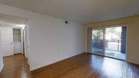 This single-floor space offers a clean, functional layout highlighted by warm hardwood flooring that extends throughout the main living area. The room is finished with crisp white walls and white trim, creating a bright and neutral backdrop well-suited for a variety of furnishing styles. A ceiling-mounted HVAC vent ensures year-round climate control, while the understated design keeps the space feeling open and uncluttered. A standout feature is the sliding glass door positioned along one wall, which floods the interior with natural light and provides direct access to a private balcony. The balcony is enclosed by a metal railing and overlooks a lush, tree-lined outdoor area, offering a pleasant connection to the outside environment. The transition between the interior hardwood floors and the balcony is seamless, reinforcing the indoor-outdoor feel. The overall ambiance is light, airy, and move-in ready, with a simple yet inviting character that makes the most of the available space.