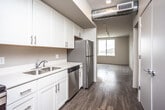 This single-floor unit presents a clean, contemporary design characterized by wood-style flooring that runs consistently throughout, neutral walls, and modern finishes. The kitchen is well-appointed with white shaker-style cabinetry, brushed nickel hardware, light countertops, and a full suite of stainless steel appliances including a refrigerator, electric range, built-in microwave, and dishwasher. An exposed cylindrical ductwork element adds an industrial accent, bridging the kitchen to the open living area beyond.

The living area is generously proportioned, featuring recessed lighting alongside a track lighting system, and benefits from natural light through large windows that frame outdoor views. A door provides direct access to an outdoor space, enhancing the overall openness of the area. The bedrooms are well-sized with wood-style flooring, neutral walls, and windows that allow natural light.

The unit includes two bathrooms, each finished with white shaker cabinetry, light countertops, and a tub-shower combination. One bathroom features a tall linen tower cabinet for additional storage. Both bathrooms maintain the consistent, clean aesthetic found throughout the rest of the unit.