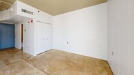 Located at 1 N Fifth Ave in downtown Tucson, Arizona, this studio unit offers an efficiently designed single-floor layout with an industrial aesthetic. The open living area features polished concrete floors and white-painted concrete block walls that lend a clean, urban character to the space. Exposed conduit along the ceiling adds to the industrial feel, while a sliding glass door floods the main area with natural light and provides views of the surrounding downtown cityscape.

The kitchen is positioned along one wall and includes a full suite of appliances — an electric range, dishwasher, and refrigerator — along with a single-basin sink, modest cabinetry with contemporary hardware, and open stainless steel shelving for additional storage. The counter space, though compact, is functional and well-organized.

A dedicated sleeping area features a double-door closet and the same concrete block wall construction, maintaining a cohesive aesthetic throughout the unit. The bathroom offers a clean, modern finish with a wall-mounted vanity, a mirrored medicine cabinet, and a combined bathtub and shower with tile surround. Concrete floors continue into the bathroom, tying together the overall design language of the space. This unit is well-suited for those seeking a minimalist, urban living environment in the heart of Tucson.